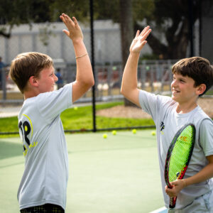Twin boys high fiving on the tennis court