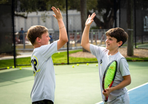 Twin boys high fiving on the tennis court